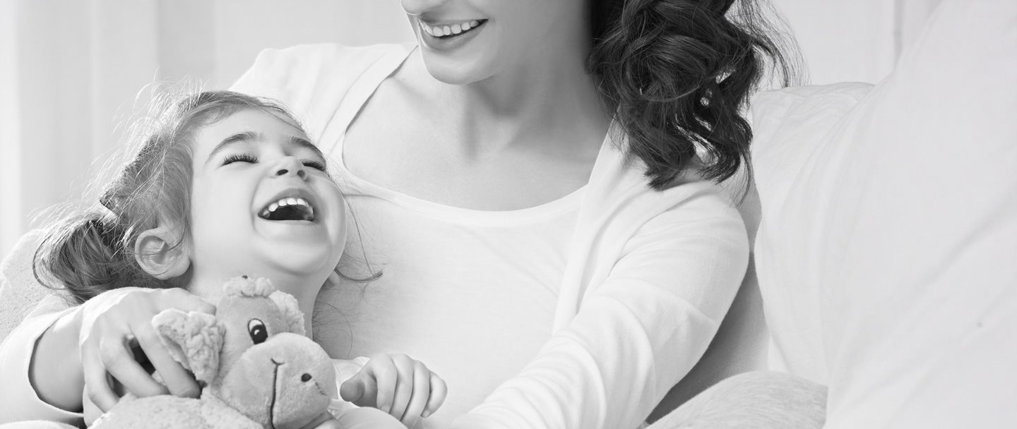 Kleine Mädchen liegt im Arm der Mutter und hält ein Stofftier.