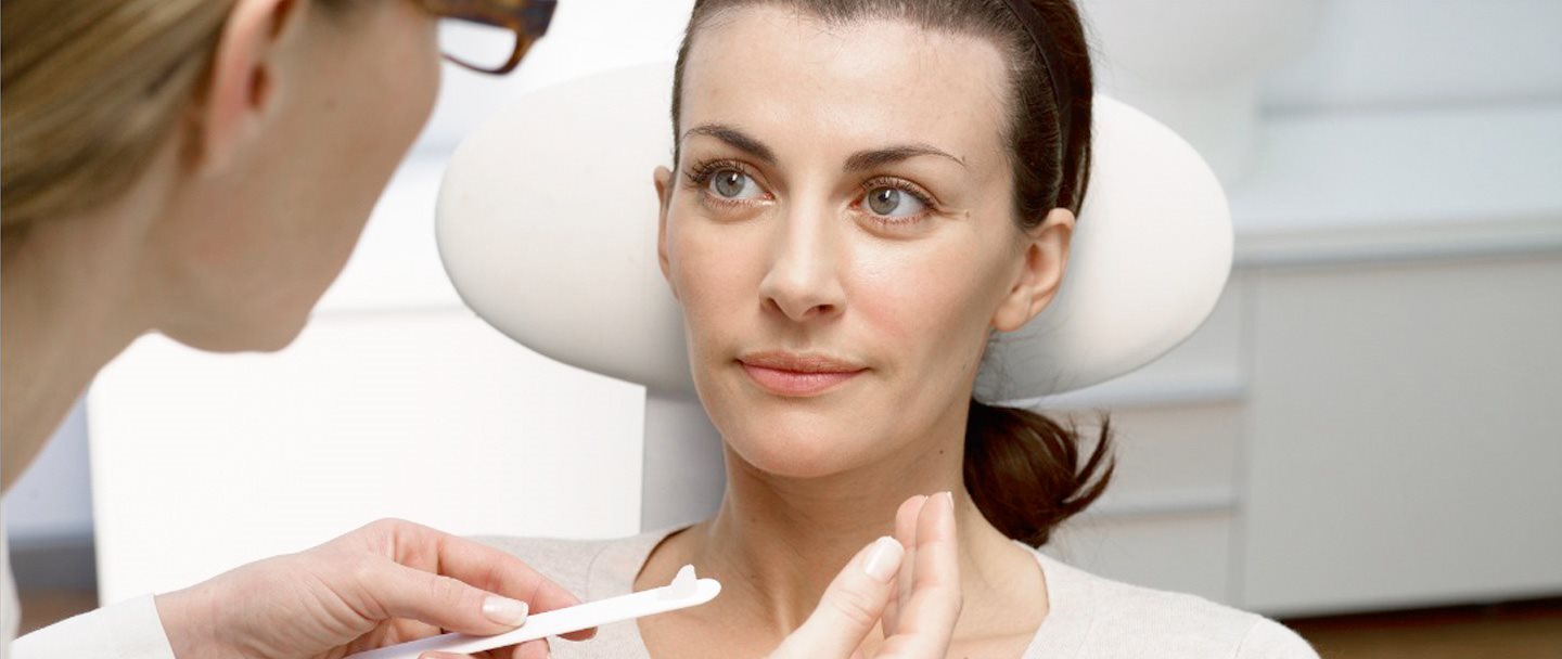 Dermatologe trägt Salbe auf Gesicht eines Patienten auf